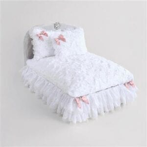 A bed with white sheets and pink bows on it.