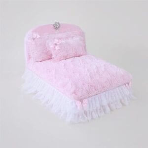 A pink bed with white ruffles and pillows.